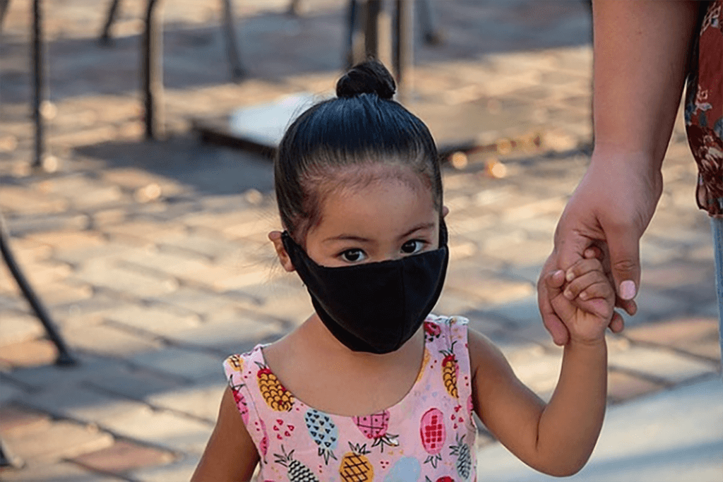 Young child with face mask holding caregiver's hand
