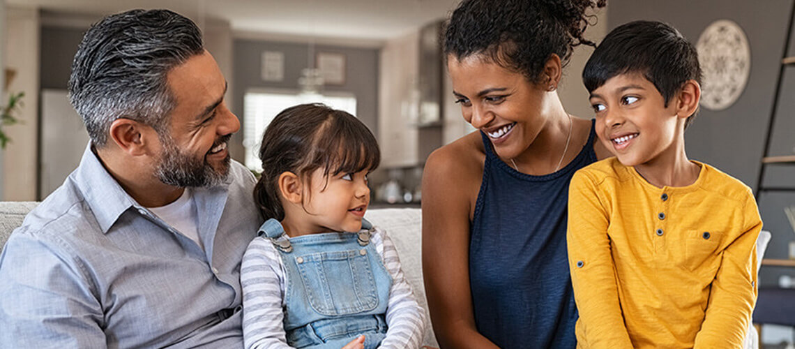 South Asian family - smiling and sitting on their couch mom and dad with young daughter and son sitting on their laps