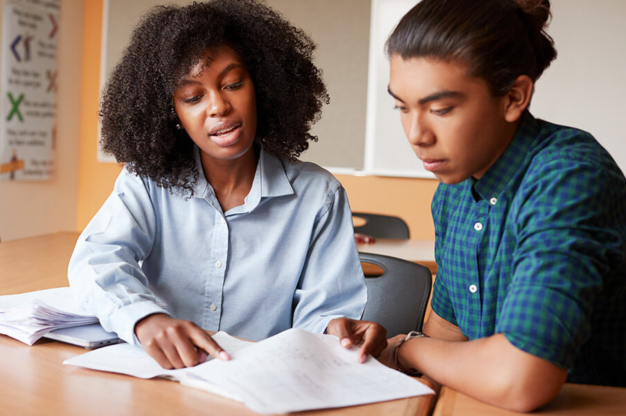 A black female teacher helps a male youth with school work