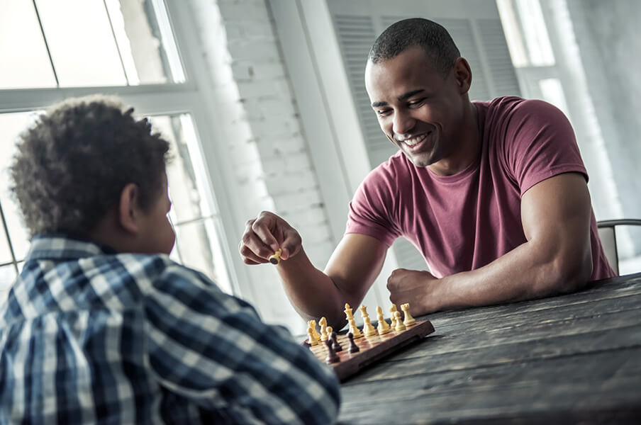 A young teen of colour is playing chess with a Youth worker/mentor