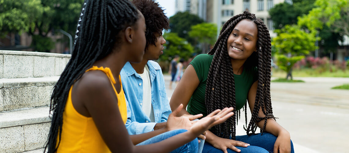 2 black teens with a black female mentor smiling and speaking together outside