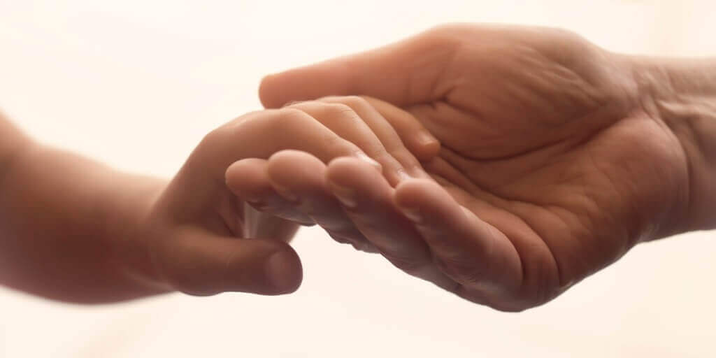 child's hand reaching for an adults had for children at the bedside