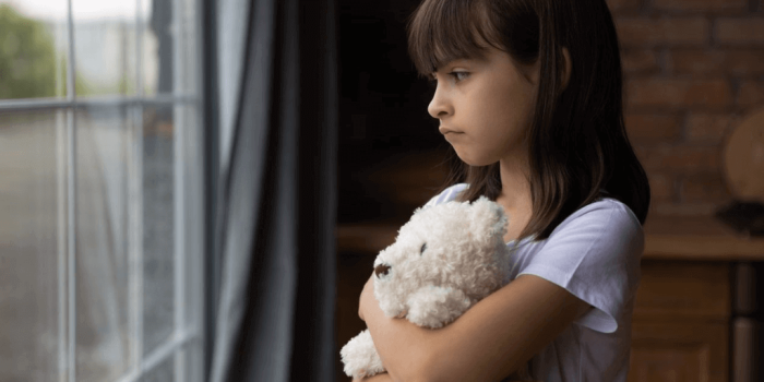 sad child holding a teddy bear looking out a window