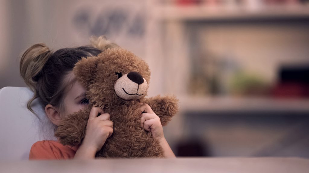 child hiding behind a teddy bear showing child anxiety