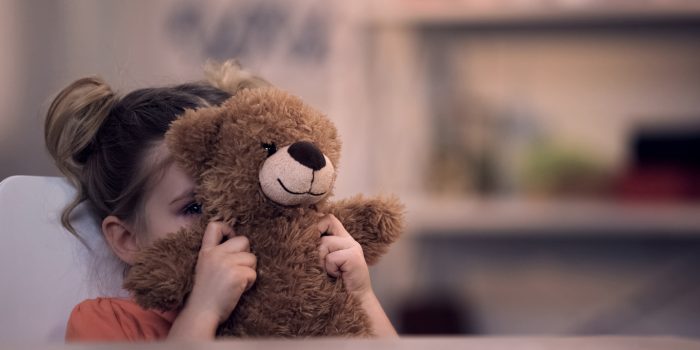 child hiding behind a teddy bear showing child anxiety