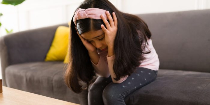 child sitting on couch holding head perhaps in pain for CBT for pain